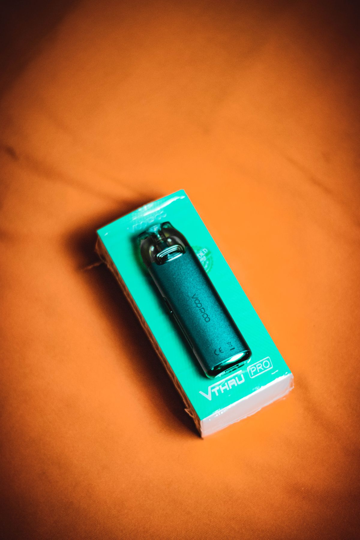 Vape-Gerät in Verpackung vor orangefarbenem Hintergrund