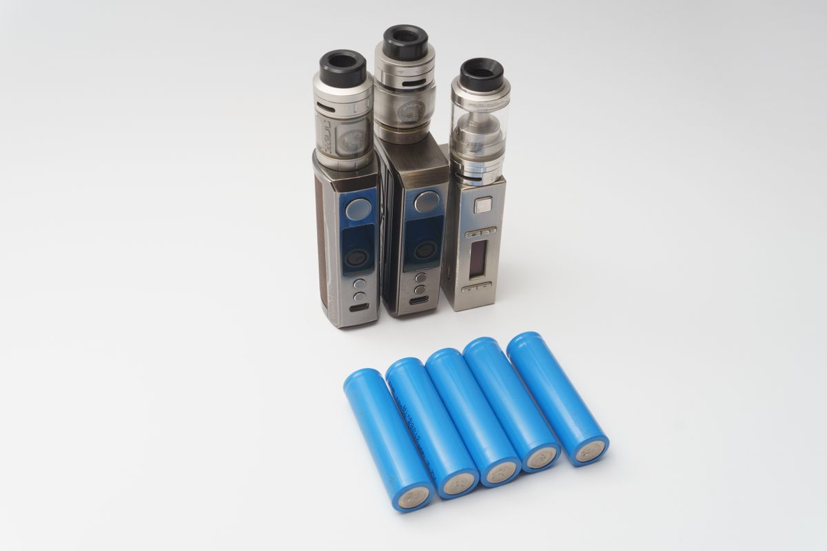 Drei Vape-Mods und mehrere 18650-Akkuzellen auf weißem Untergrund