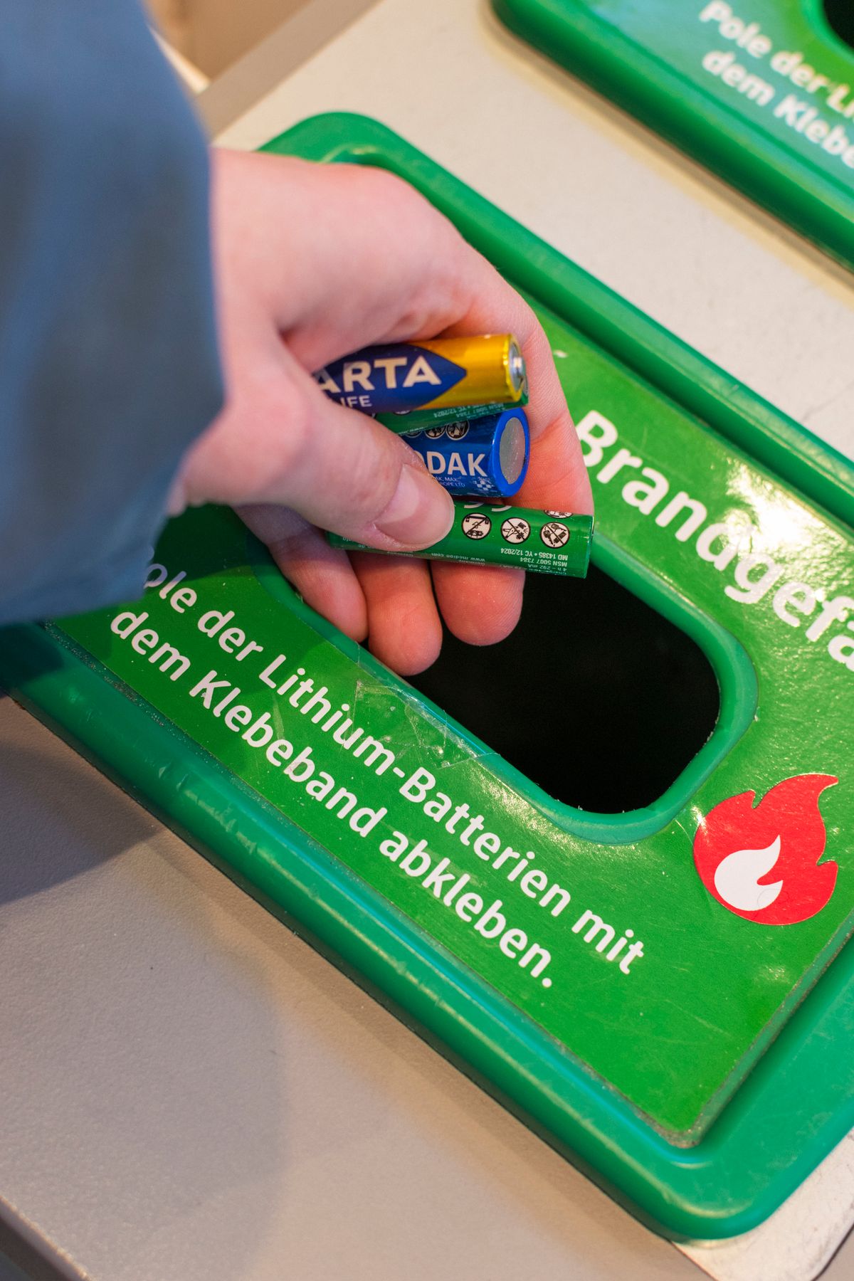 Symbolbild: Person entsorgt Batterien in einer Recycling-Sammelbox