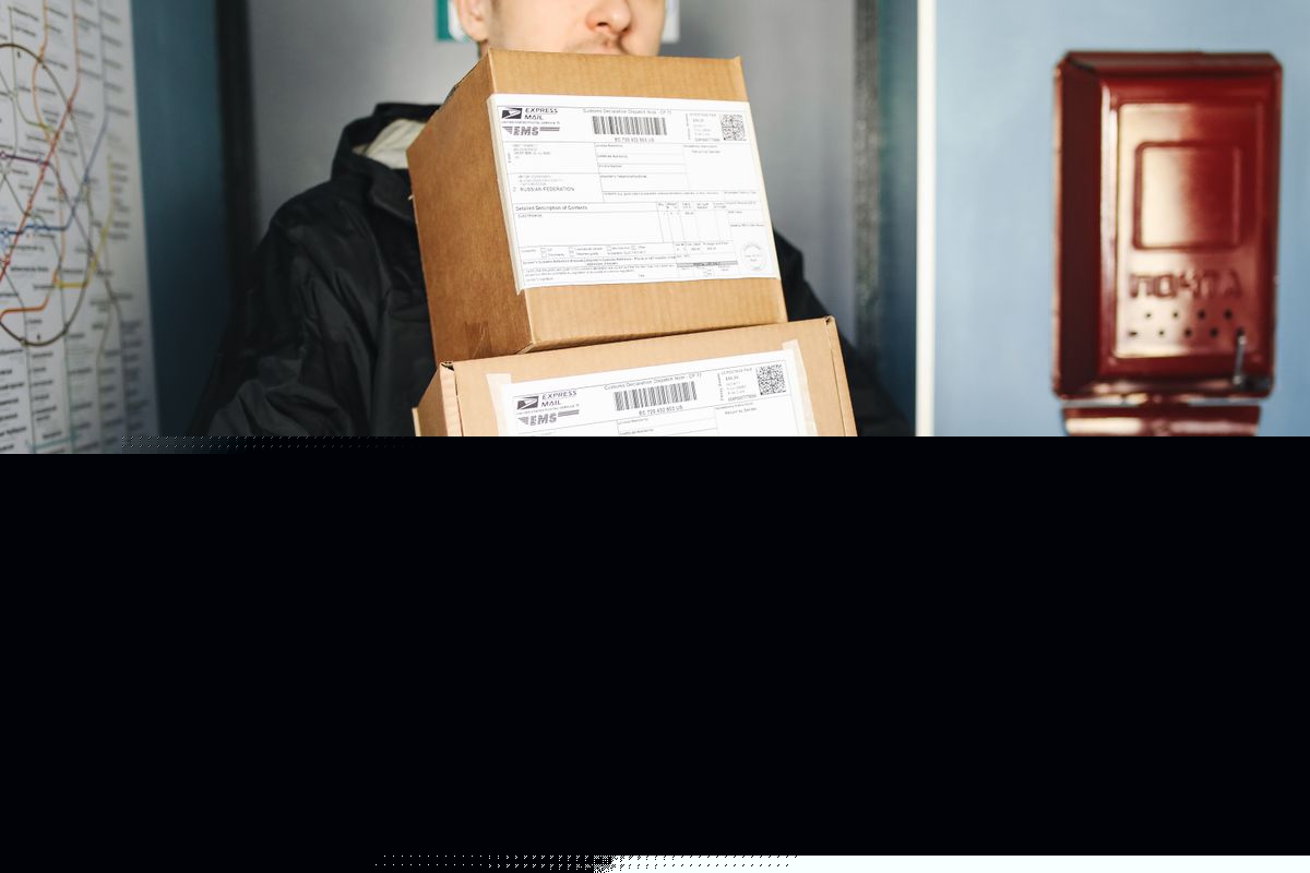 Symbolbild: Kurier trägt gestapelte Kartons im Innenbereich